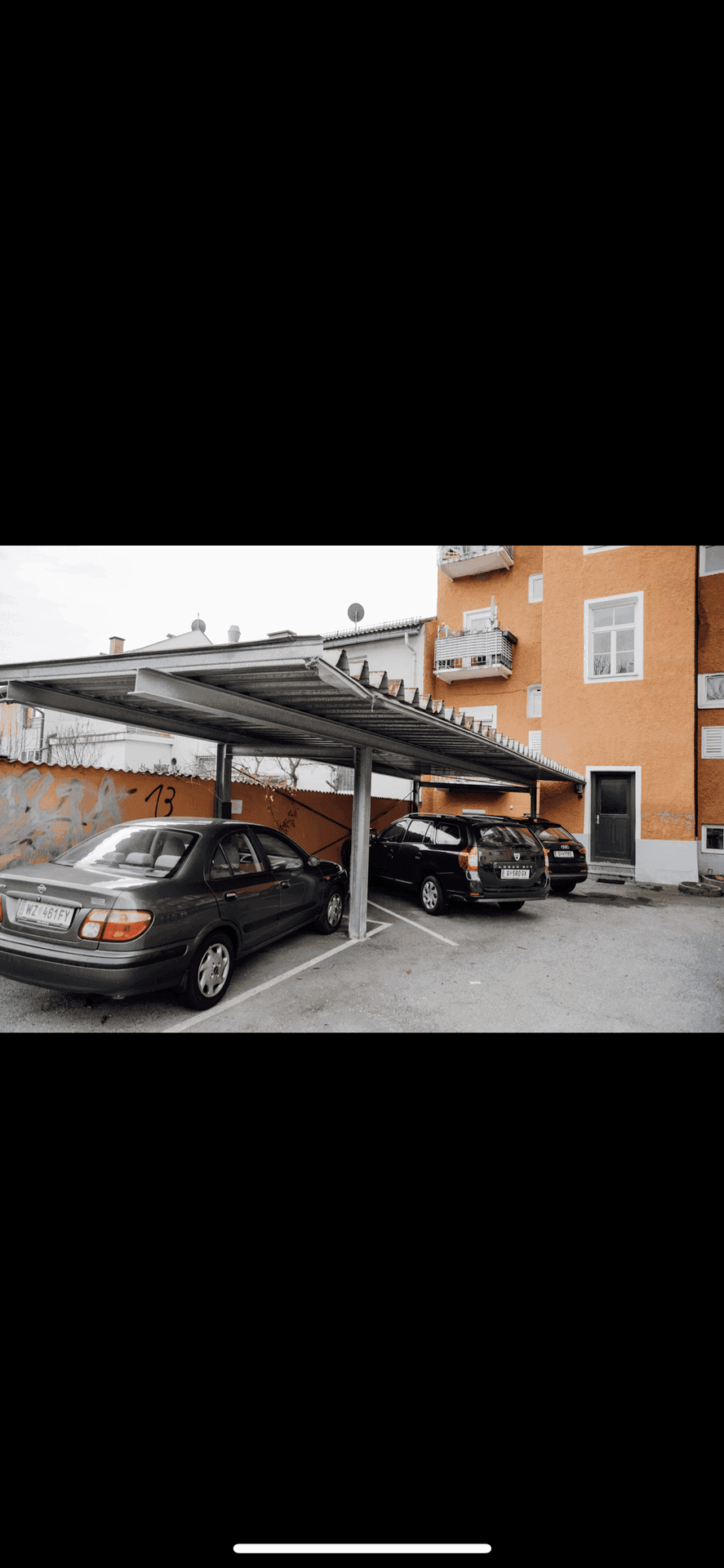 Überdachte Parkplätze vor einem Wohngebäude mit orangefarbener Fassade.