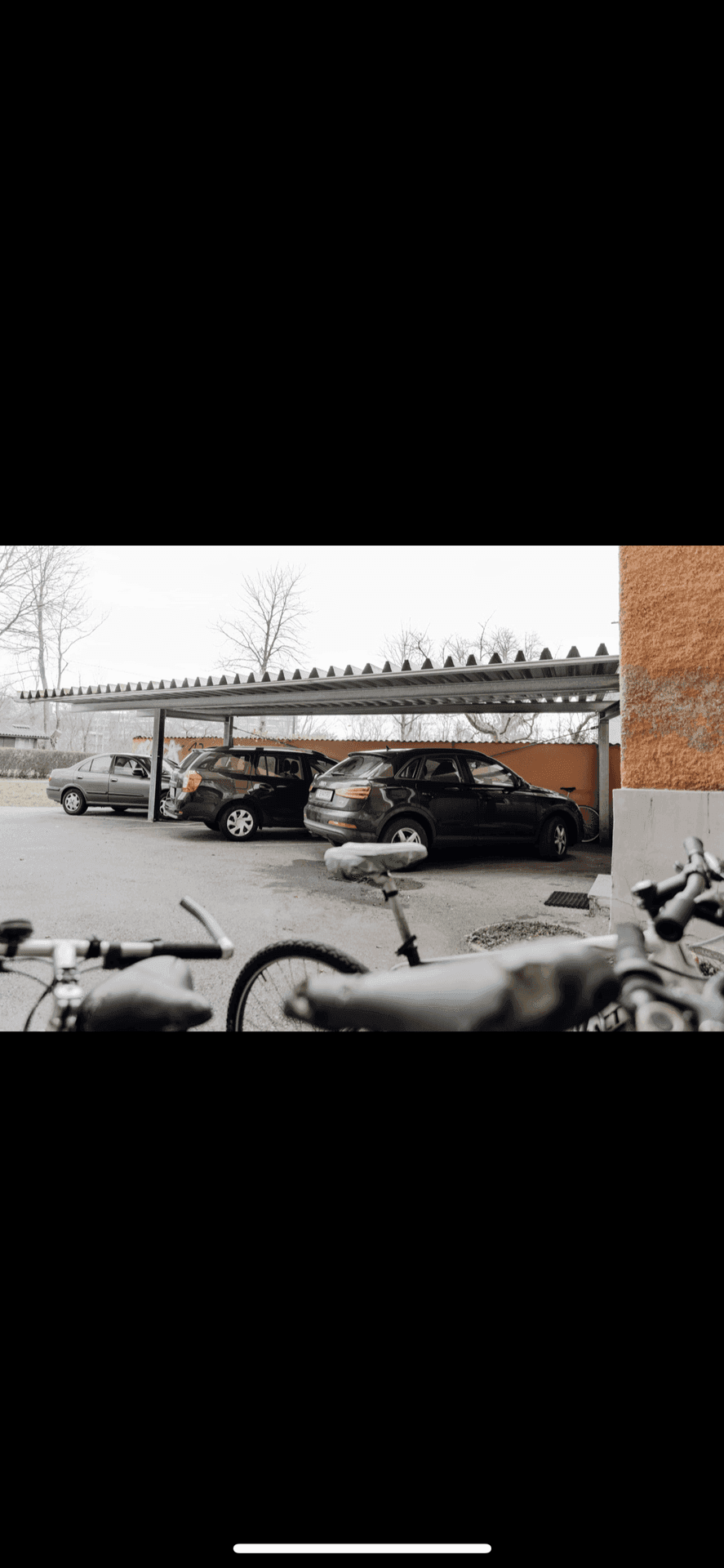 Außenansicht des Gebäudes mit überdachten Parkplätzen und einem Fahrrad im Vordergrund.