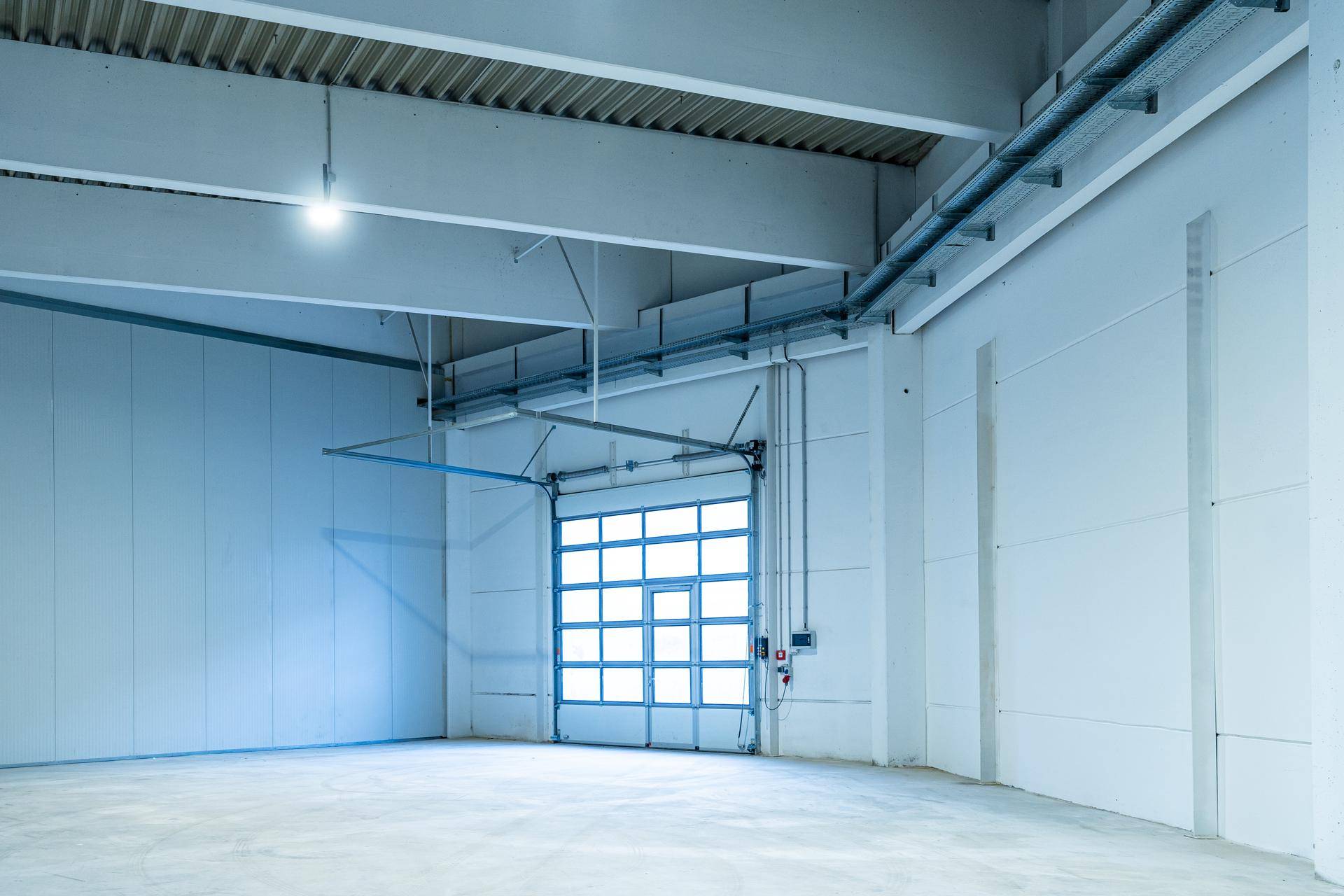 Helle Lagerhalle mit großem Rolltor, Betonboden und sichtbaren Installationen an der Decke.