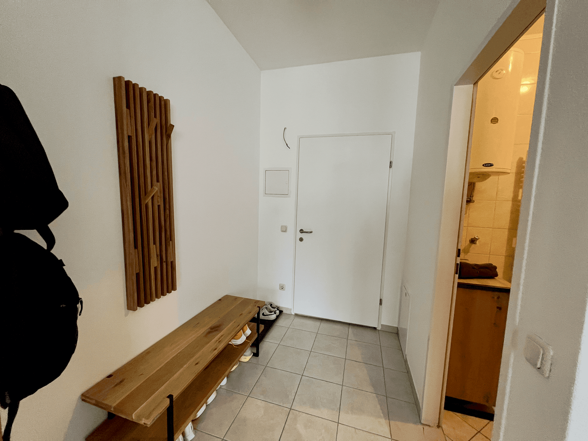Heller Eingangsbereich mit Holzsitzbank und Garderobe, gefliestem Boden und Zugang zum Bad.