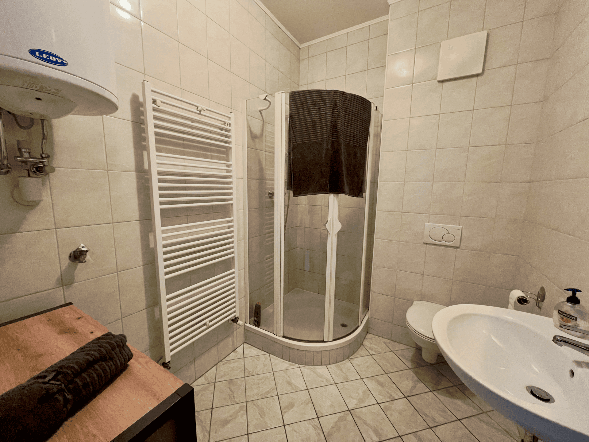 Funktionales Badezimmer mit Eckdusche, WC, Waschbecken und Handtuchheizkörper, komplett gefliest.