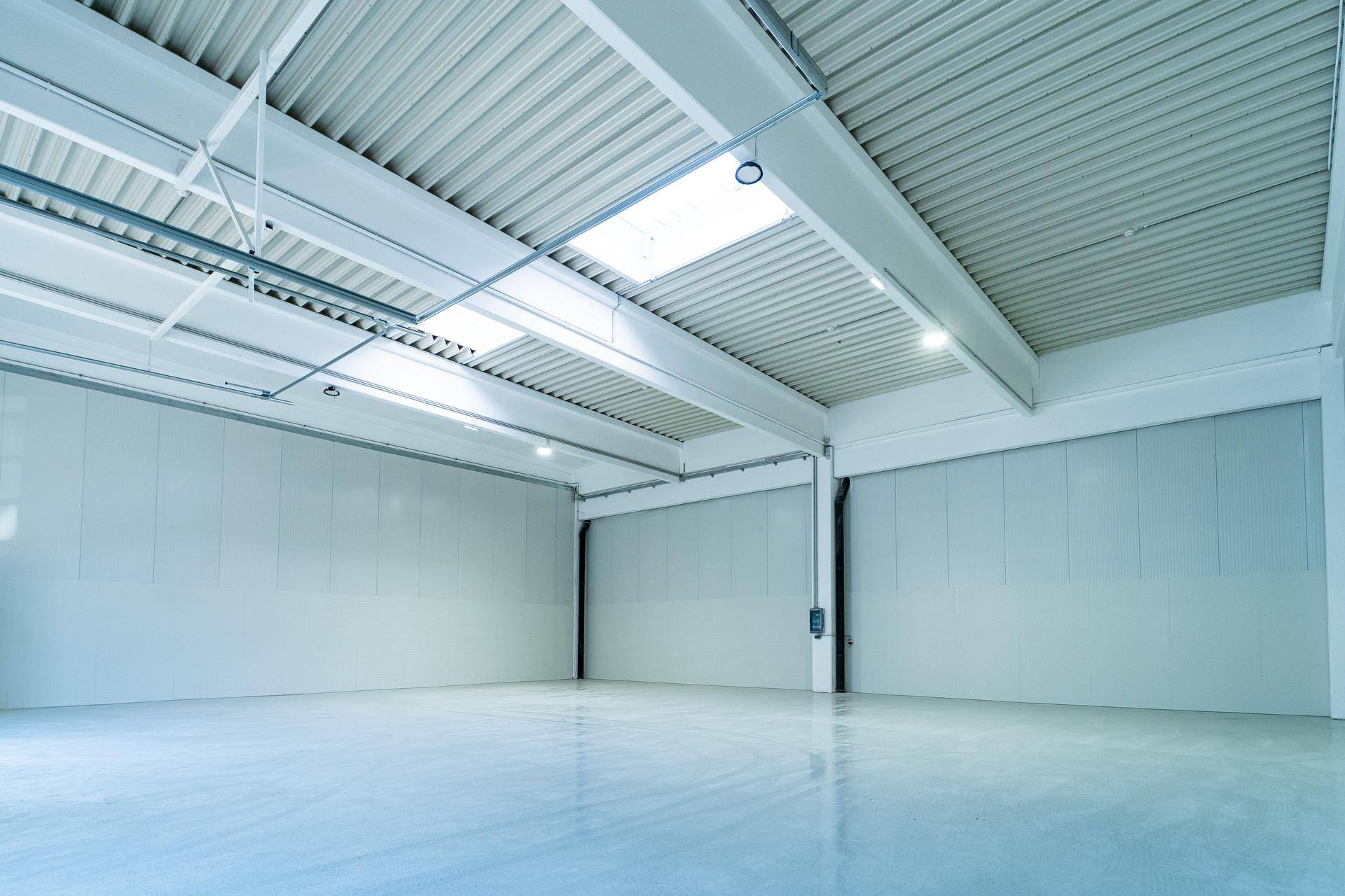 Helle und saubere Lagerhalle mit glänzendem Betonboden, hohen Decken und Oberlichtern für Tageslicht.