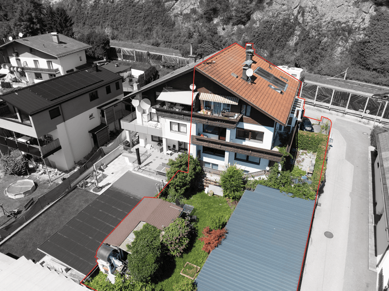 Luftaufnahme eines Wohnhauses mit rotem Dach und angrenzendem Gartenbereich, umrandet von einer roten Linie.