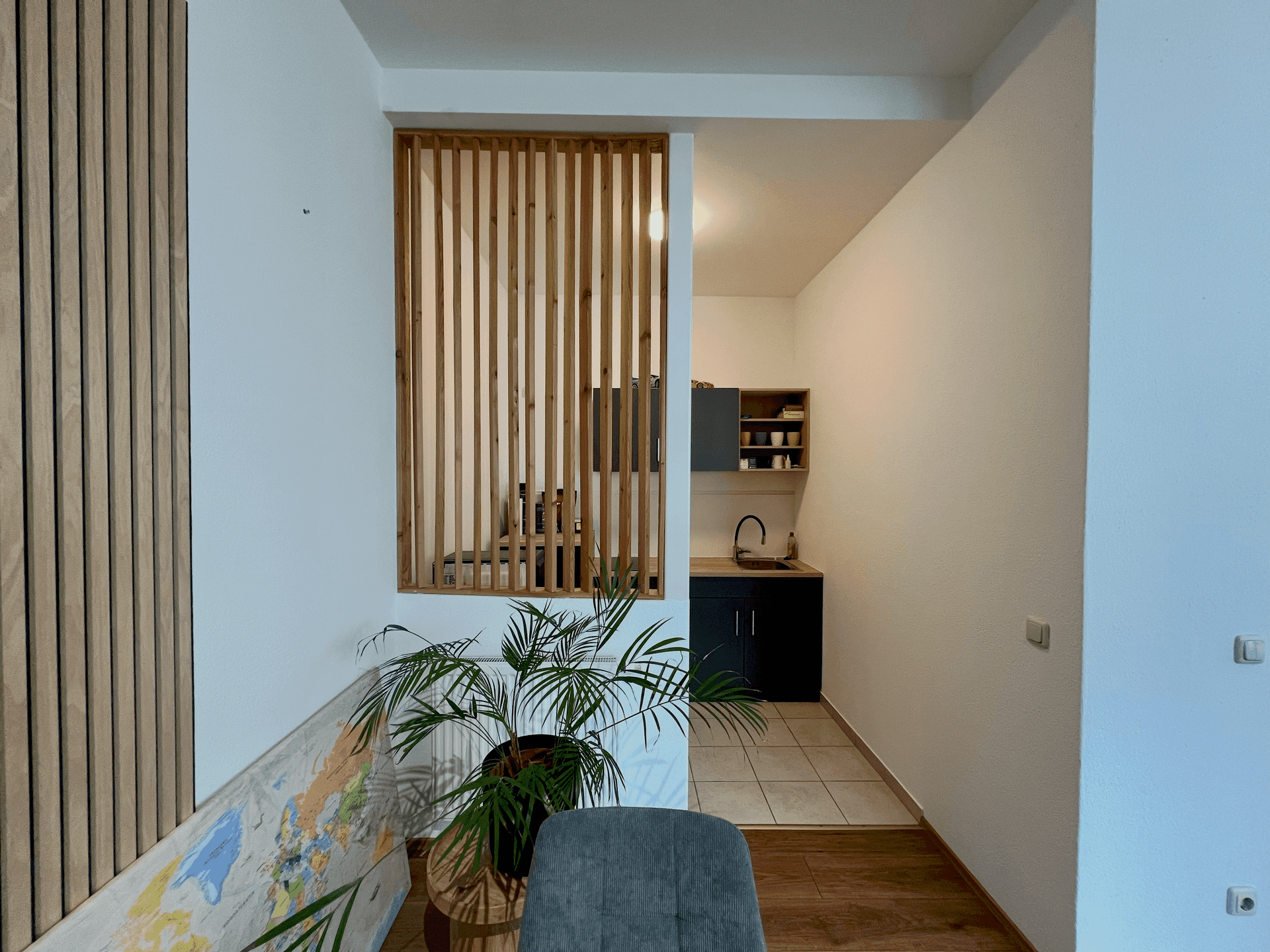 Blick durch eine Holzlamellenwand in eine kleine, funktionale Küchenzeile mit Spüle.