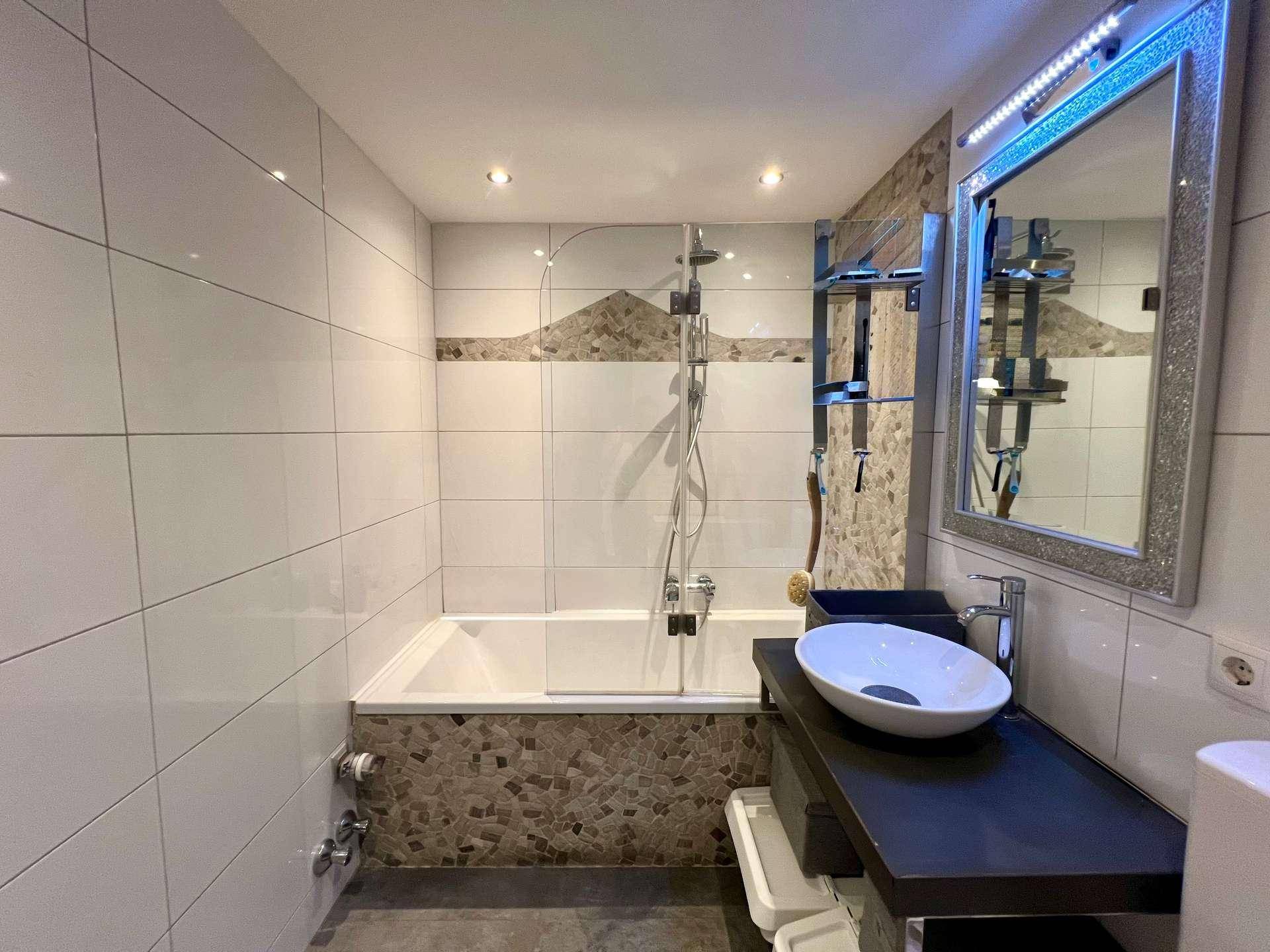 Modernes Badezimmer mit Badewanne, Duschfunktion, Einzelwaschbecken und Fliesen in Weiß und Braun.