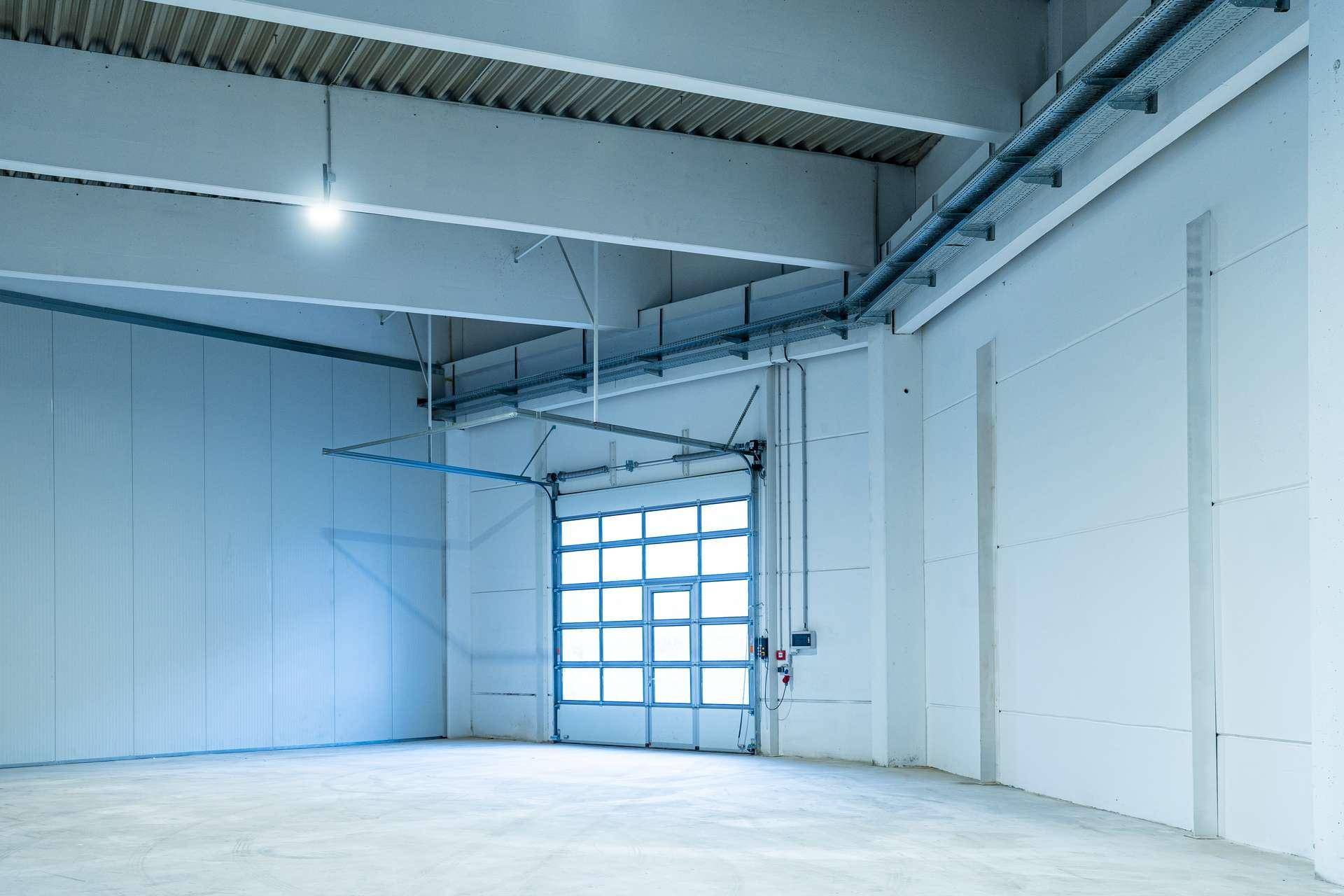 Innenansicht einer Lagerhalle mit einem großen Rolltor und sichtbaren Installationen an der Decke.