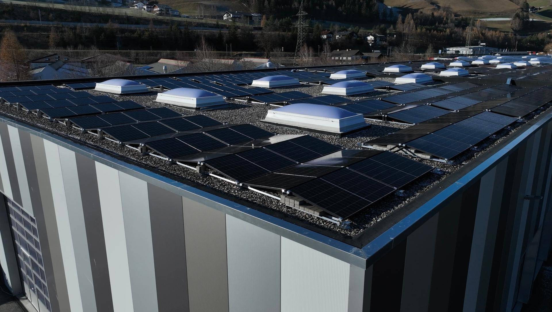 Dach eines modernen Gewerbegebäudes mit zahlreichen Photovoltaik-Modulen und Oberlichtern.