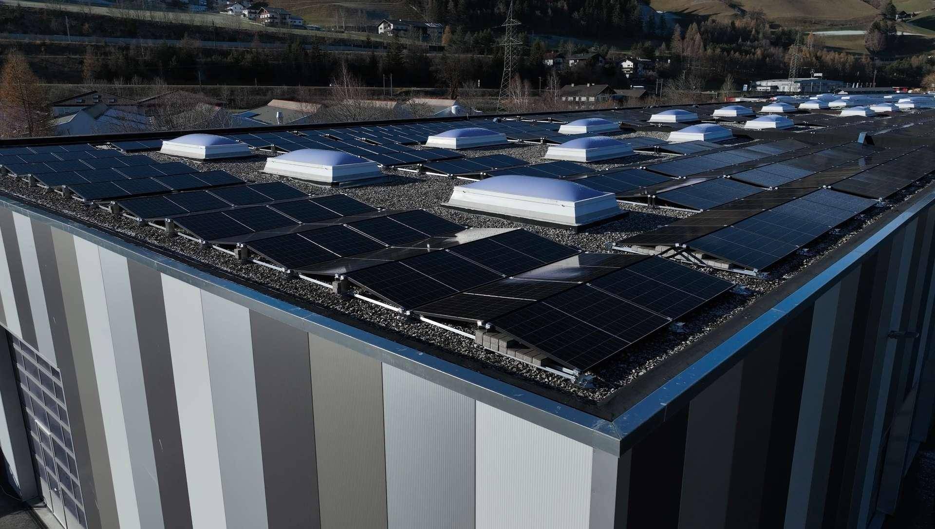 Dach eines modernen Gewerbegebäudes mit zahlreichen Photovoltaik-Modulen und Oberlichtern.