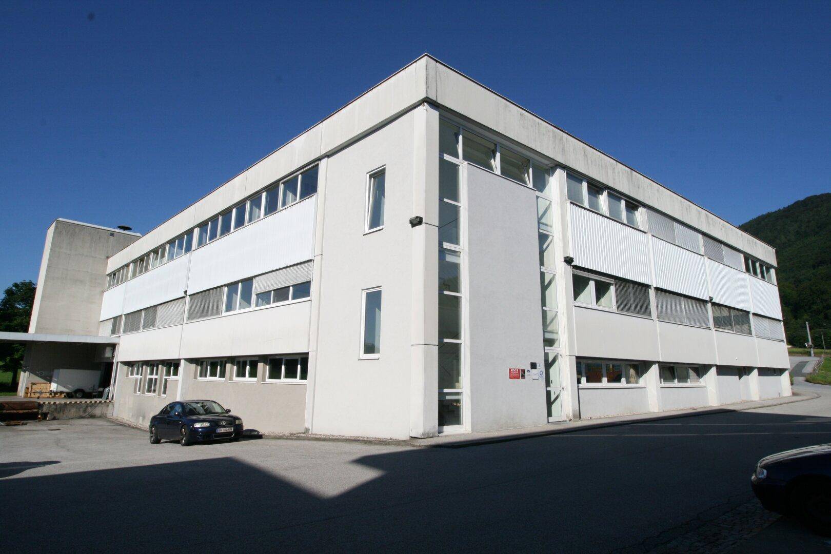 Ansicht eines modernen Bürogebäudes mit klaren Linien, vielen Fenstern und einem hellen Äußeren unter blauem Himmel.