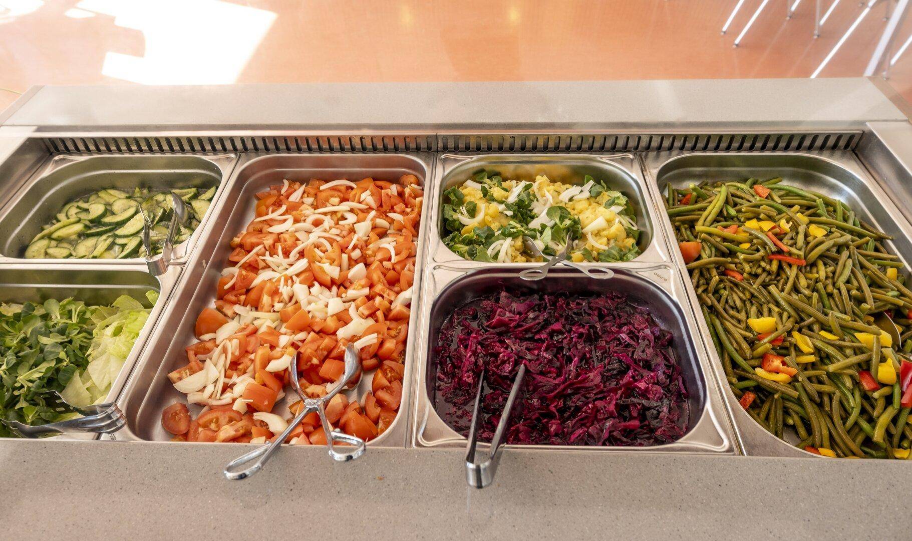 Reichhaltiges Salatbuffet mit frischen Zutaten in einer modernen Kantinenküche.