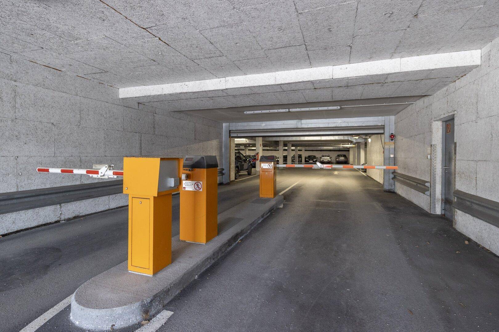 Einfahrt zu einer Tiefgarage mit Schranken und Ticketautomaten.