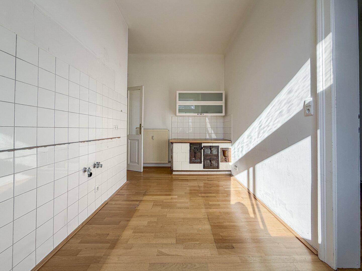 Geräumige Küche mit Holzboden, weißen Wandfliesen und einem alten Küchenschrank.