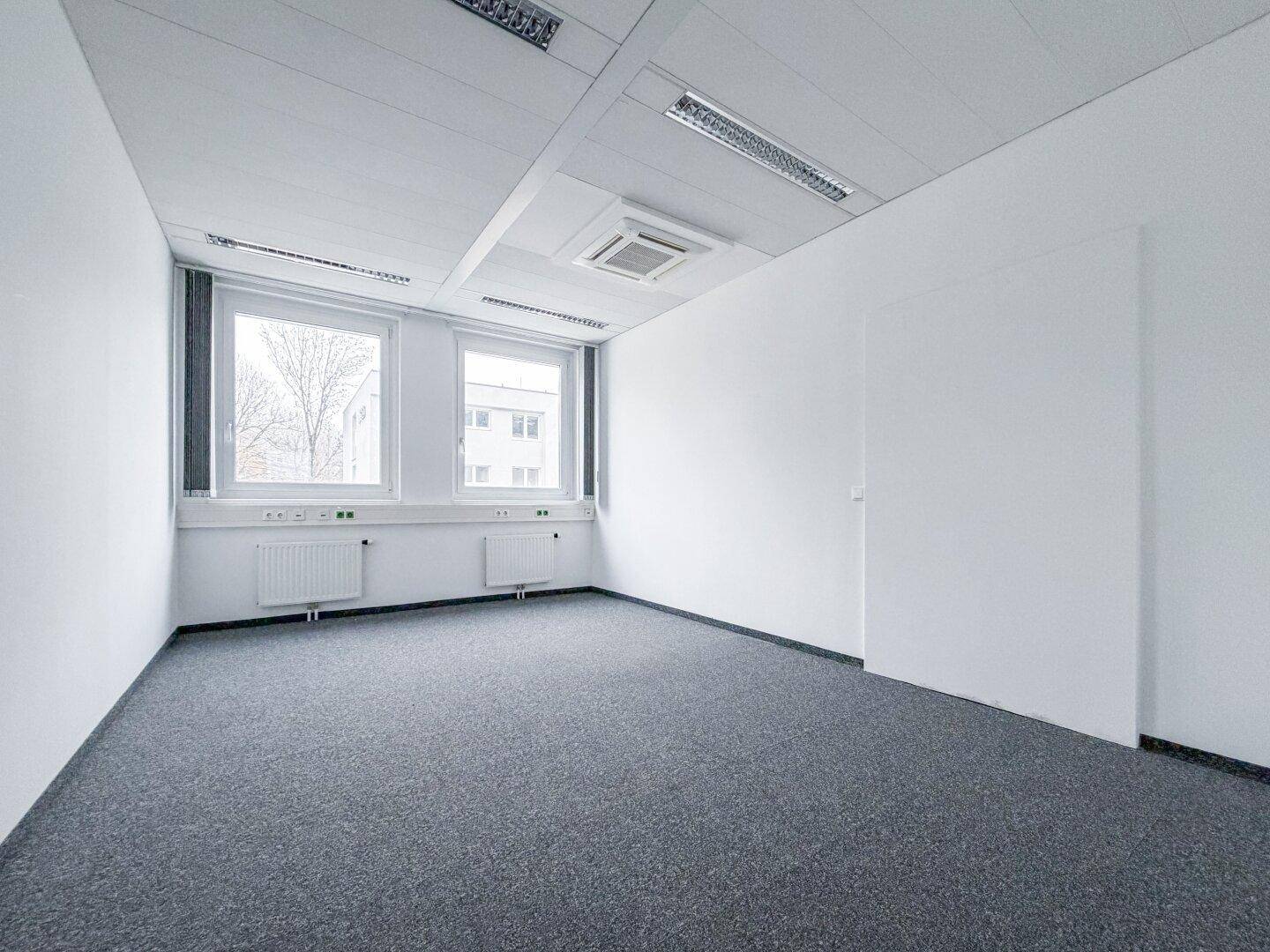 Heller Büroraum mit grauen Teppichboden und weißen Wänden, bereit zur individuellen Gestaltung und Einrichtung.