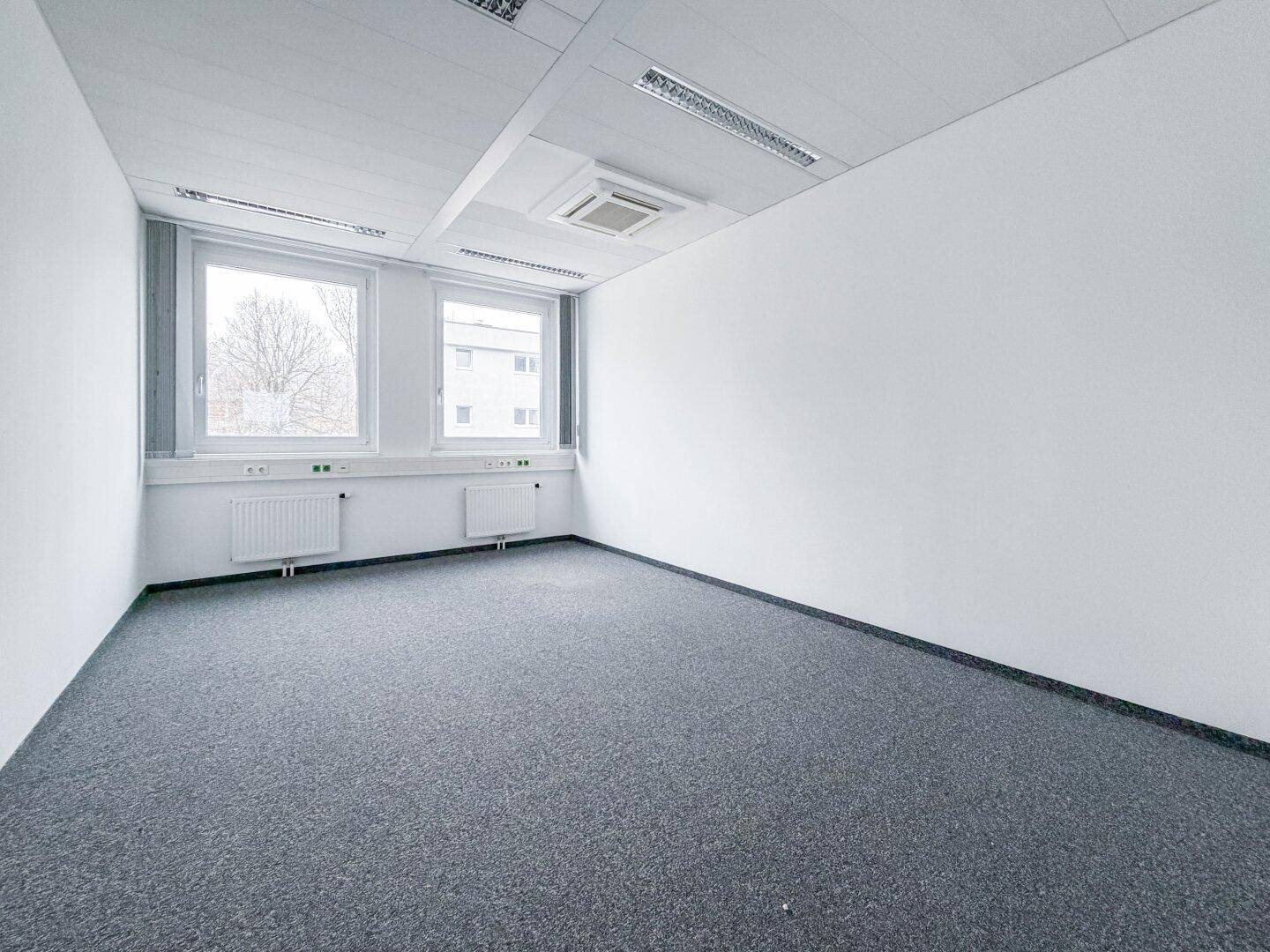 Kleinerer Büroraum mit zwei großen Fenstern, die eine helle und freundliche Atmosphäre schaffen, ideal für Einzelbüros.