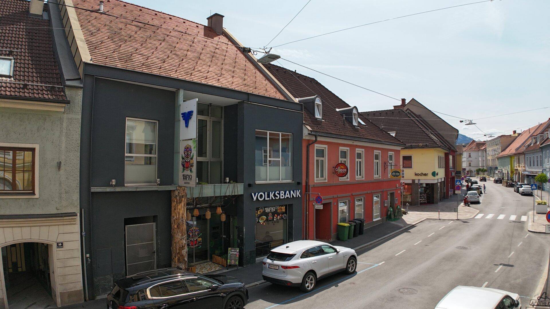 Blick auf eine belebte Straße mit Geschäften und Wohngebäuden unter blauem Himmel und Sonnenschein.