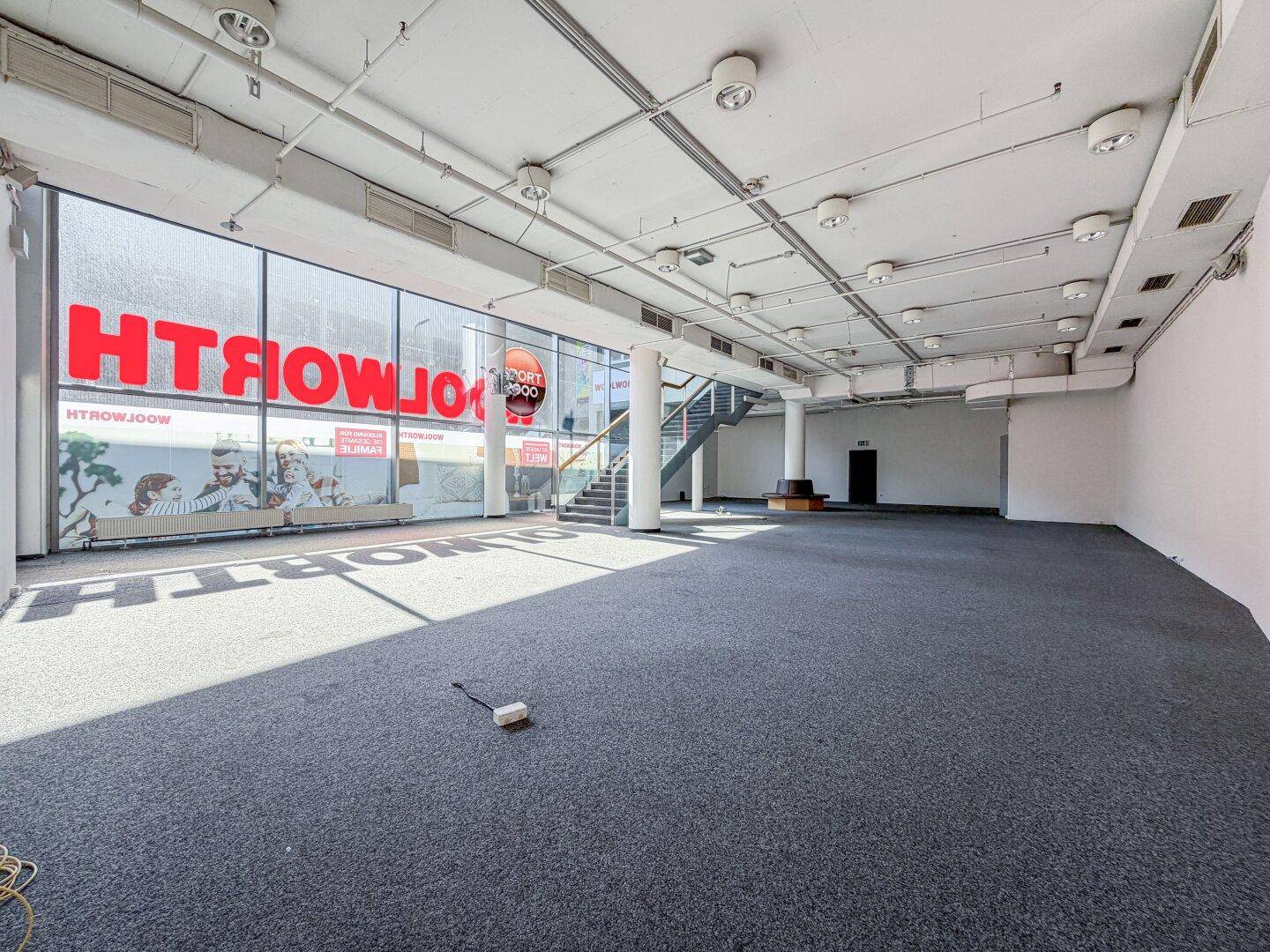 Heller, weitläufiger Gewerberaum mit großen Fenstern, Teppichboden und viel Tageslicht.
