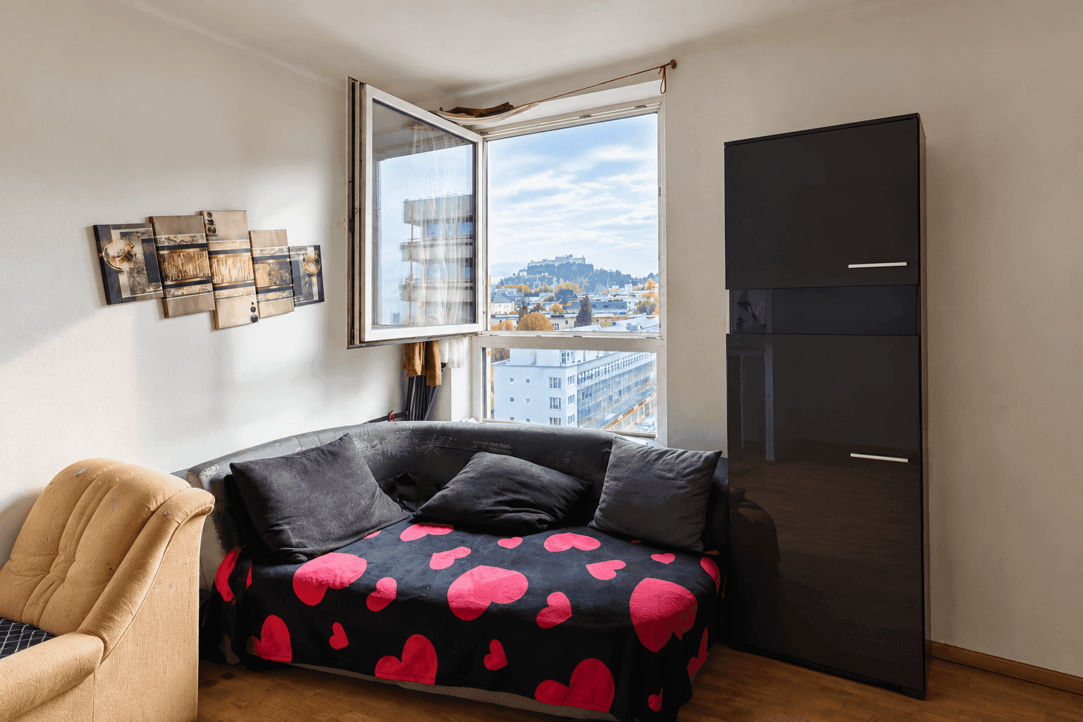 Gemütliches Wohnzimmer mit Sofa, Schrank und Blick aus dem Fenster auf die Stadt.