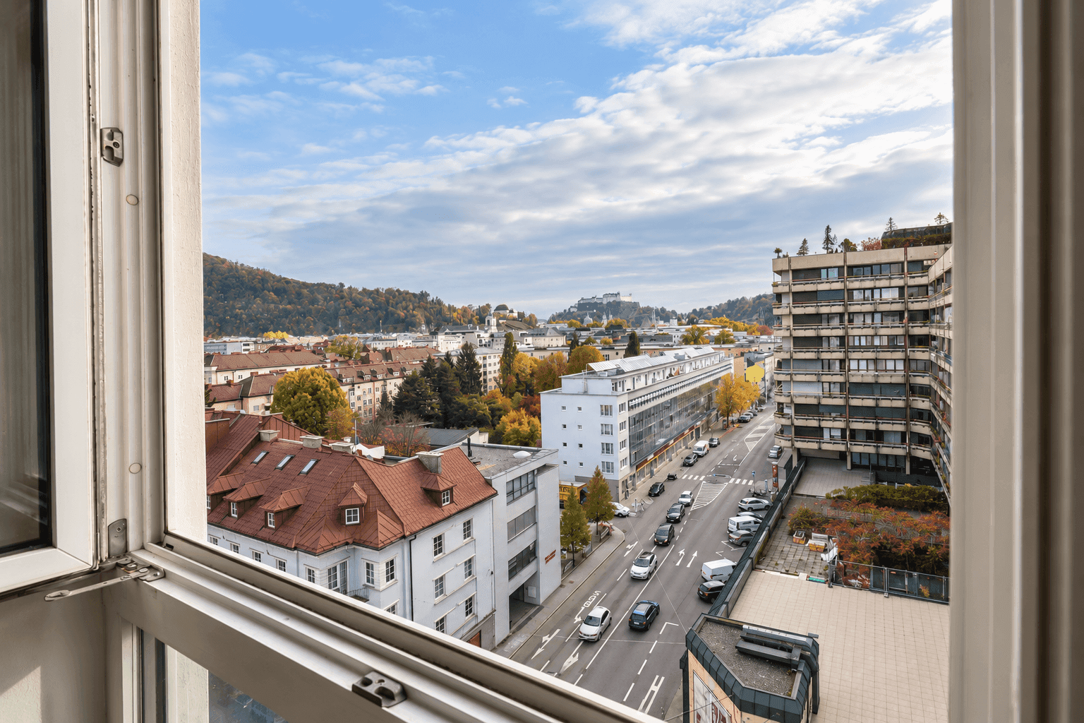 Weitblick aus dem Fenster über die Stadt mit Gebäuden, Straßen und bewaldeten Hügeln.