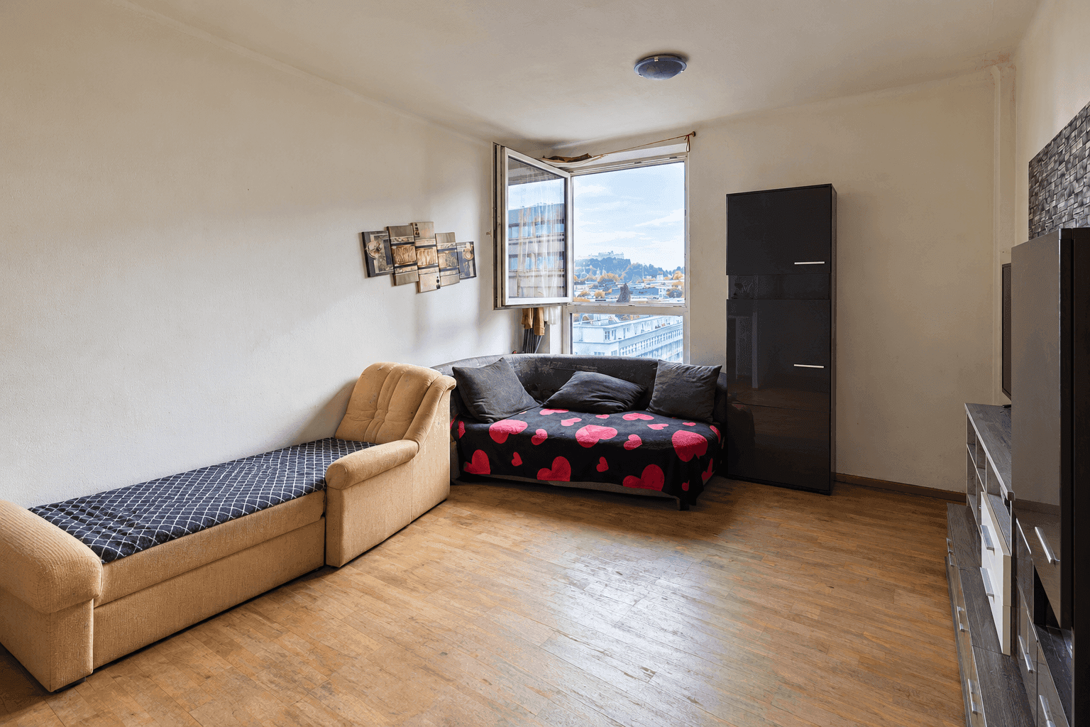 Helles Wohnzimmer mit Holzboden, Schlafsofa und Blick auf die Stadt durch das Fenster.