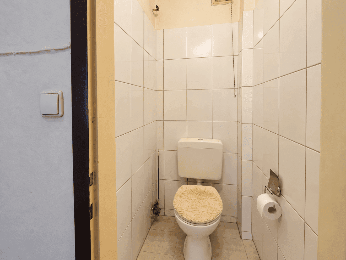 Kleines WC mit weißen Fliesen, Toilette und einem Toilettenpapierhalter an der Wand.