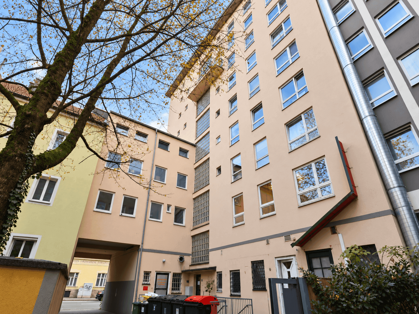 Rückansicht eines Wohngebäudes mit mehreren Fenstern und einem Durchgang zum Innenhof.