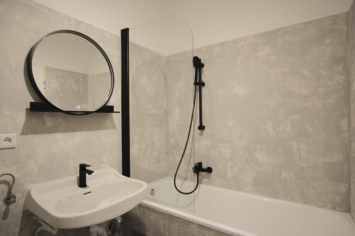 Modernes Badezimmer mit Badewanne, Duschwand, Waschtisch und beleuchtetem Rundspiegel.