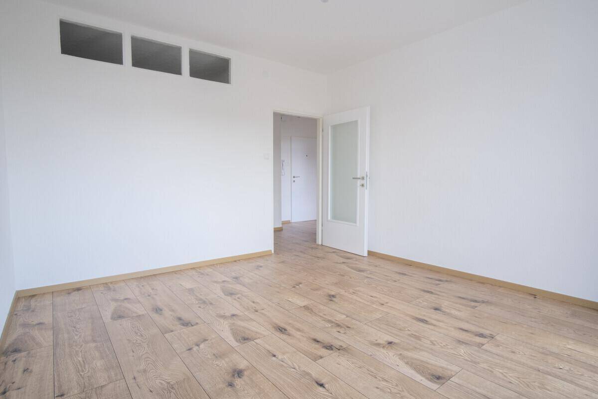Geräumiges Zimmer mit Holzboden und Zugang zu weiteren Räumen, ideal für Schlaf- oder Arbeitszimmer.