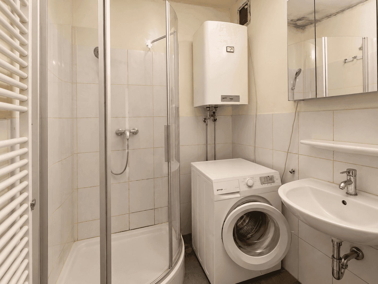 Badezimmer mit Duschkabine, Waschmaschine, Waschbecken und beheiztem Handtuchhalter.