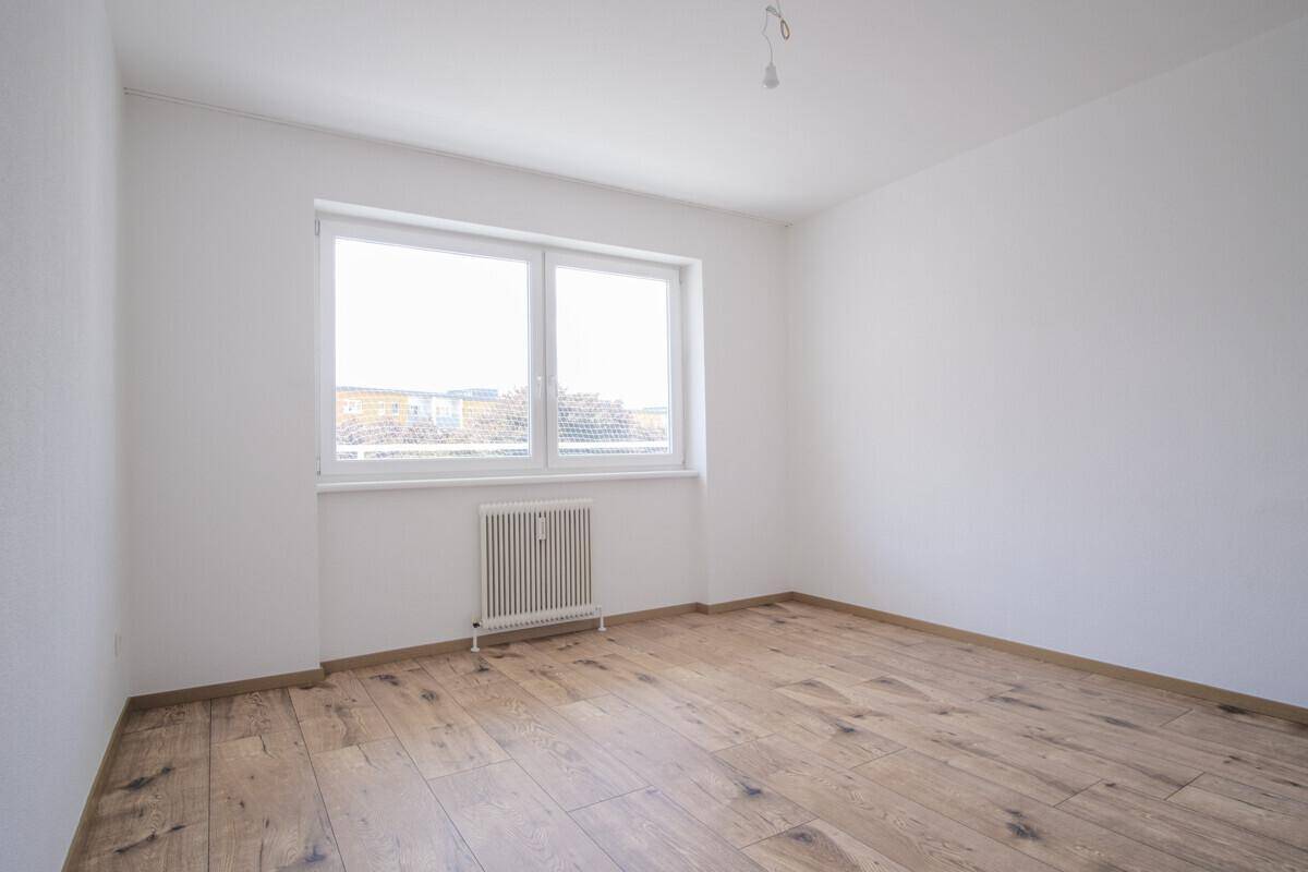 Lichtdurchflutetes Zimmer mit Holzboden und großem Fenster, bietet eine angenehme Wohnatmosphäre.
