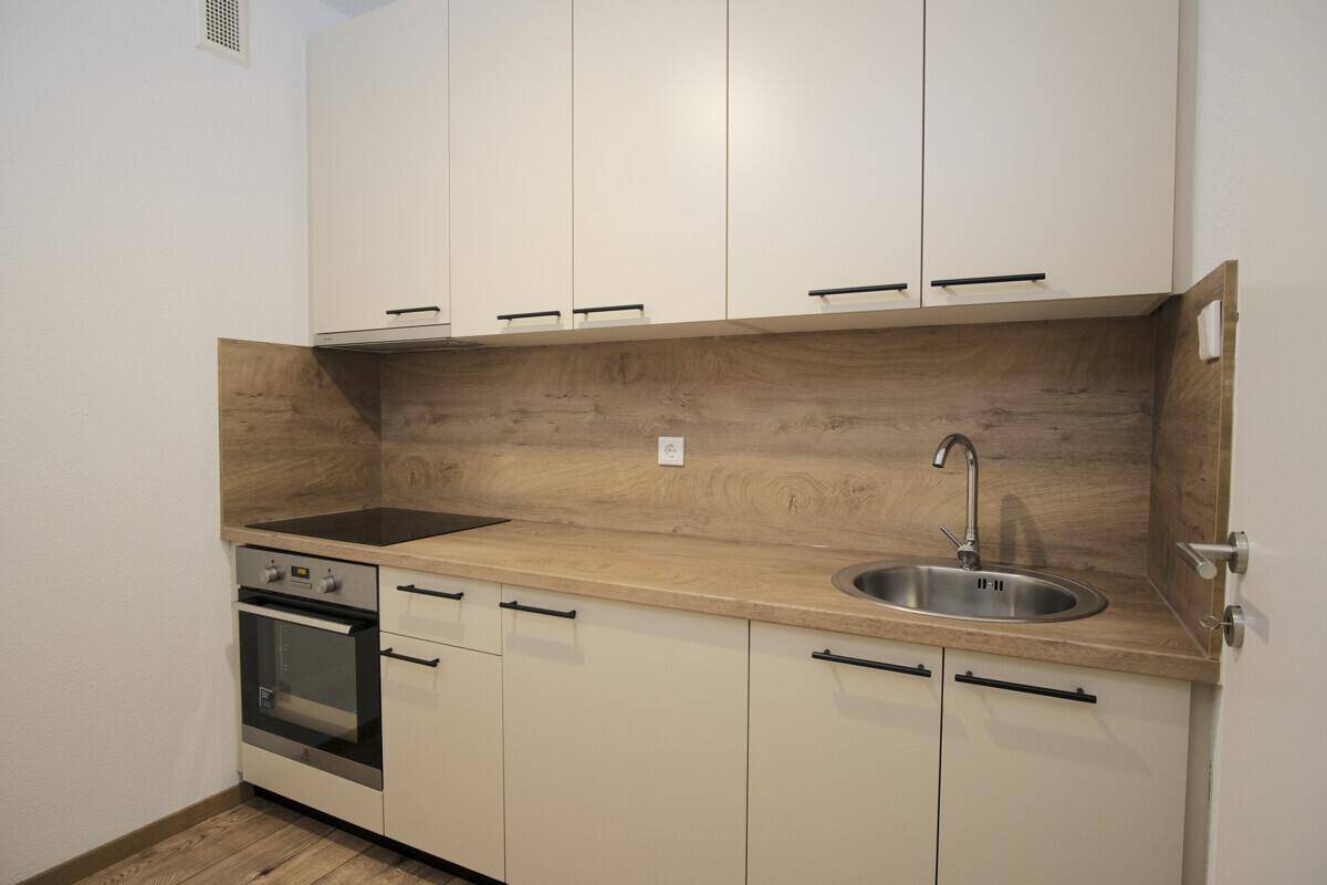 Moderne Küchenzeile mit hellen Schränken, Holzoptik-Arbeitsplatte und integrierten Geräten.