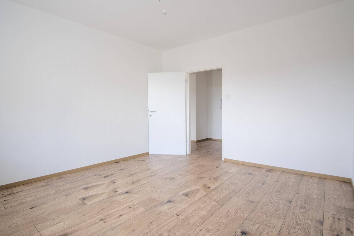 Unmöbliertes Zimmer mit hellem Holzboden und weißer Wandgestaltung, bereit zum Einzug.