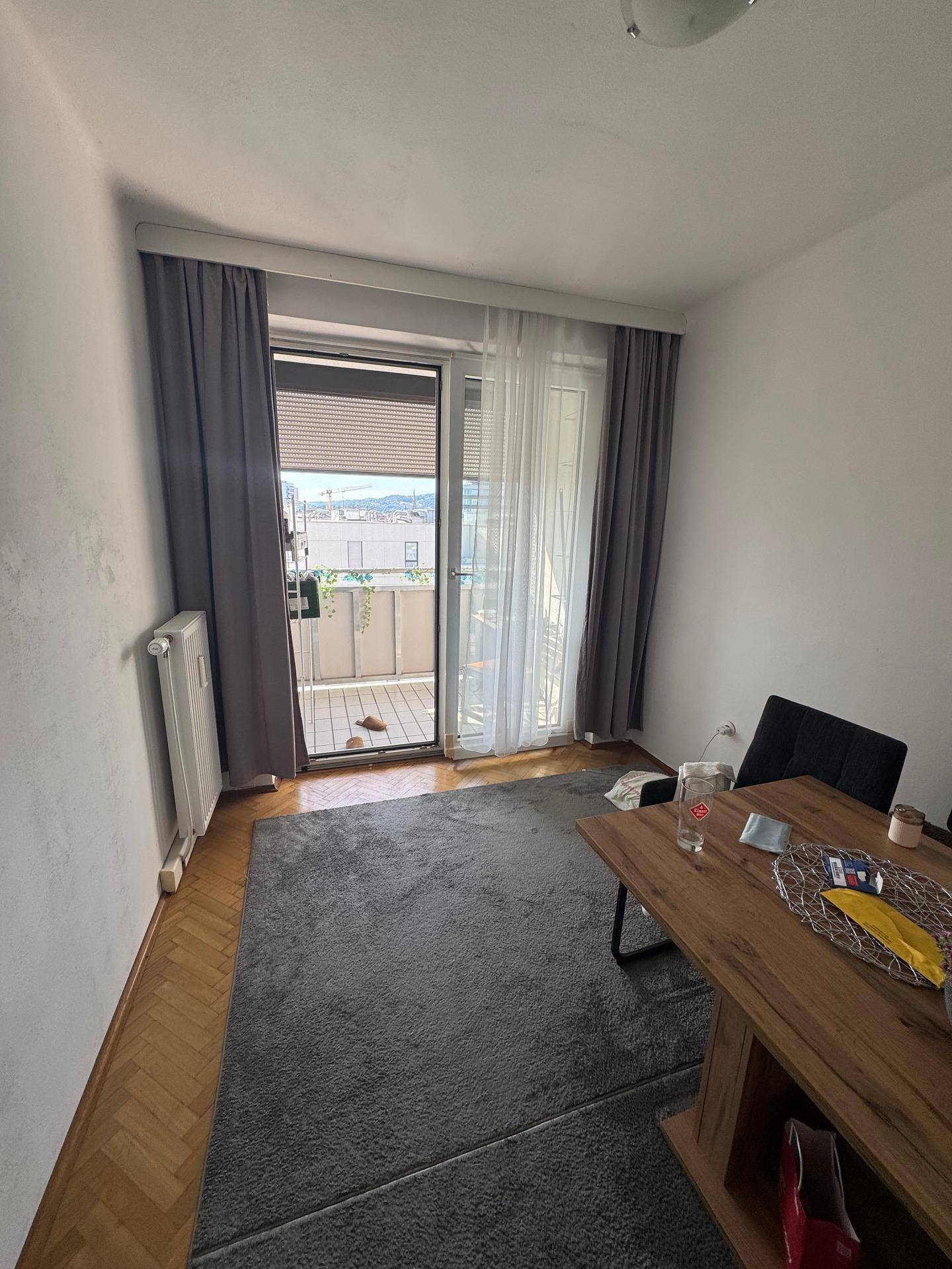 Gemütlicher Wohnbereich mit Holztisch, Teppich und Zugang zum Balkon.