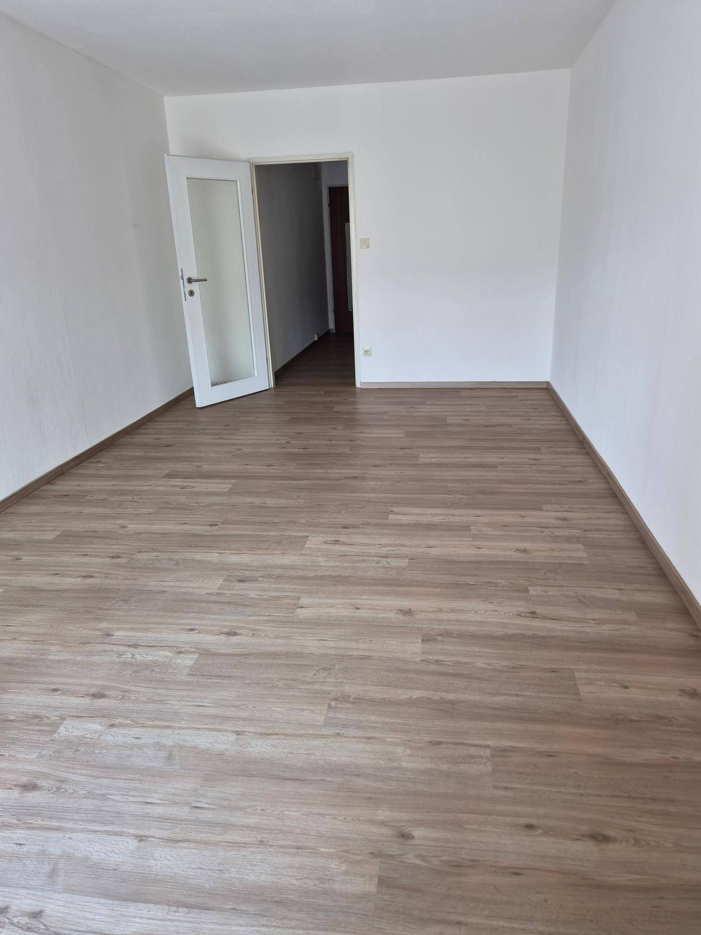 Geräumiger Raum mit Laminatboden und weiß gestrichenen Wänden, ideal als Wohn- oder Schlafzimmer.