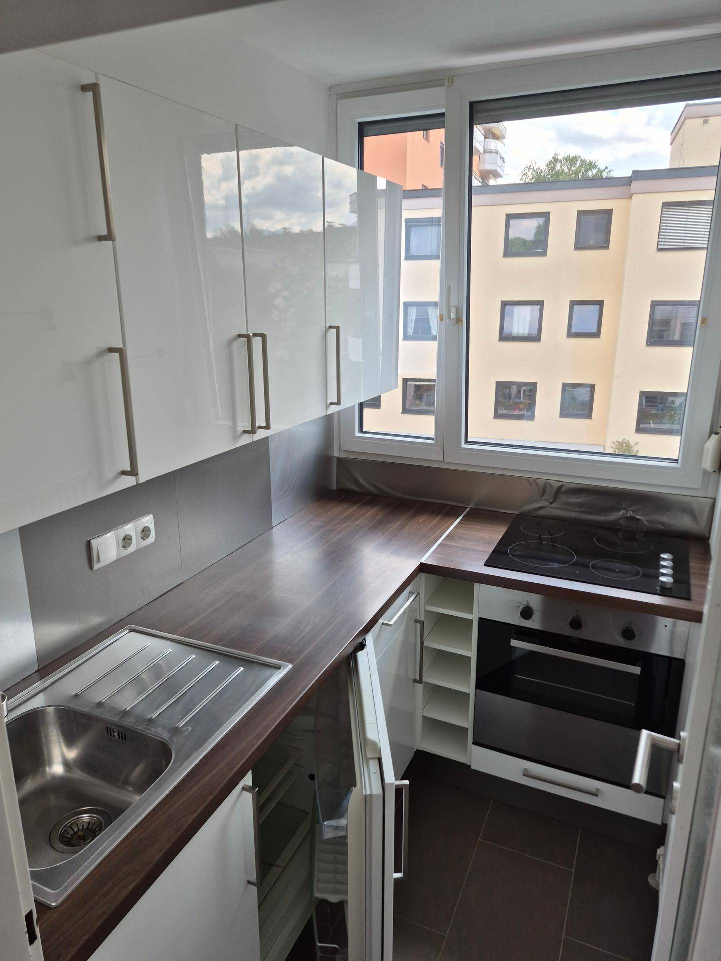 Moderne Einbauküche mit weißen Hochglanzschränken, Holztheke und Fensterblick auf die Umgebung.