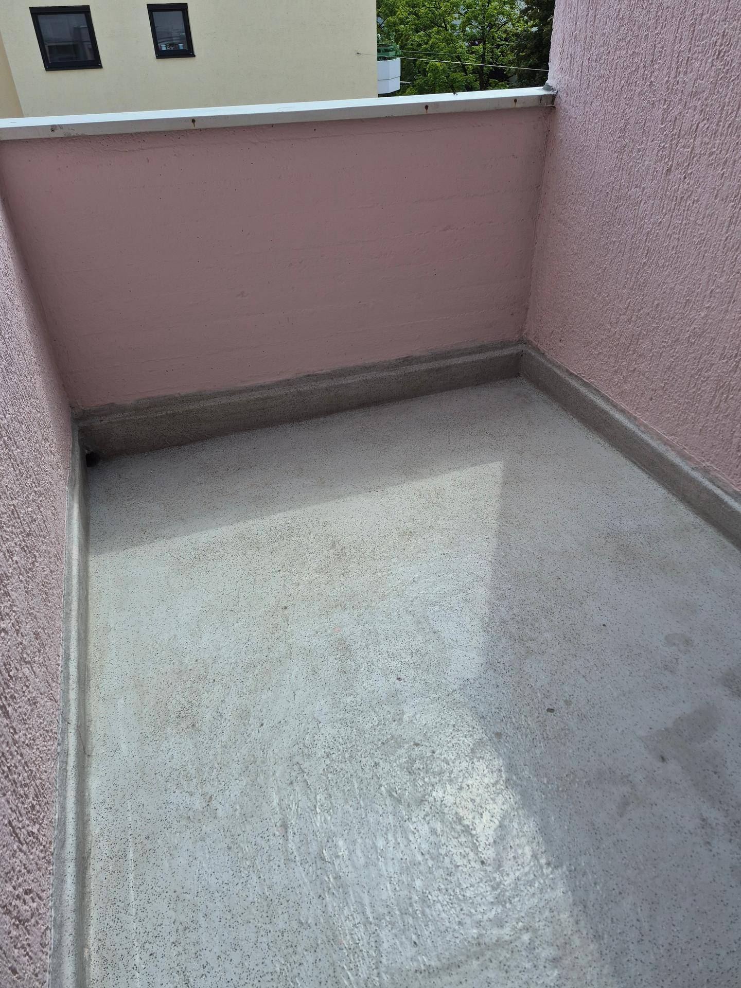 Leerer Balkon mit rosa gestrichenen Wänden und Betonboden, bereit zur individuellen Gestaltung.