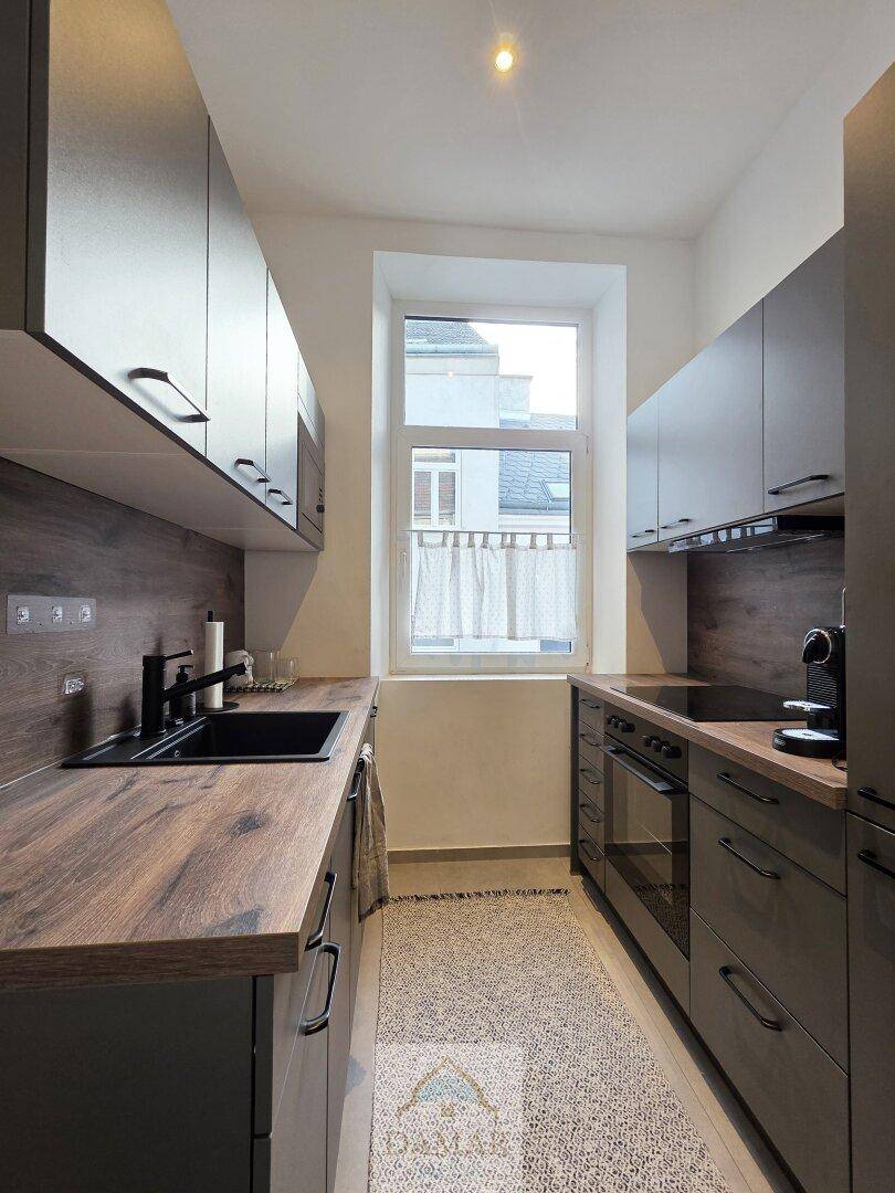 Funktionale Küche mit grauen Schränken, Holz-Arbeitsplatten und einem Fenster, das Tageslicht hereinlässt.