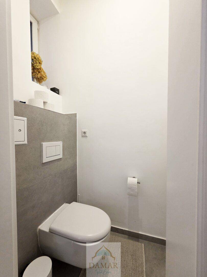 Separates WC mit wandhängender Toilette und grauen Fliesen, praktisch und platzsparend gestaltet.