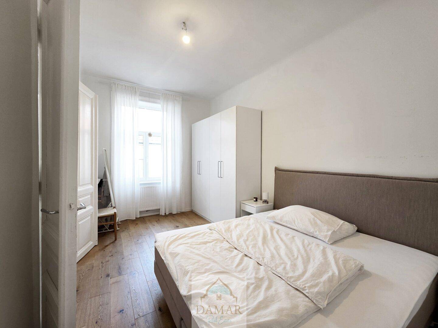 Schlafzimmer mit großem Fenster, weißen Vorhängen und geräumigem Kleiderschrank, bietet viel Stauraum.