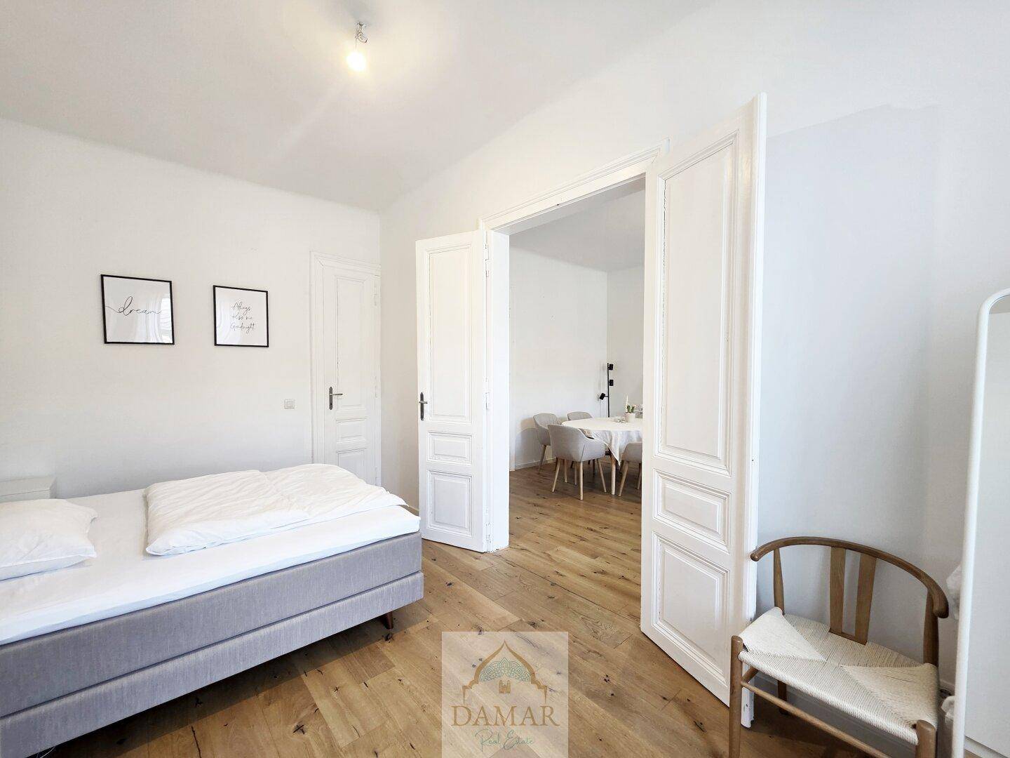 Helles Schlafzimmer mit Einzelbett und Holzboden, das durch eine offene Tür zum Wohnbereich führt.