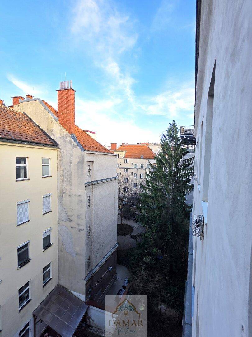 Blick von oben auf einen Innenhof mit Bäumen und umliegenden Gebäuden unter blauem Himmel.