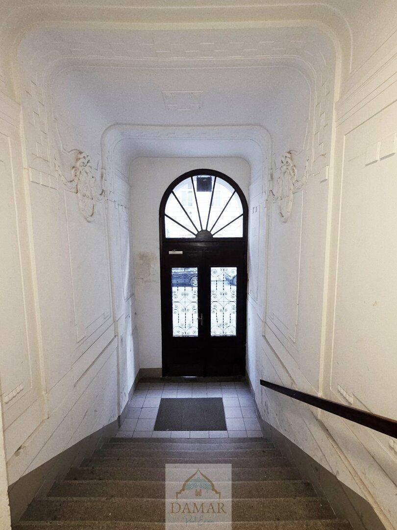 Historisches Treppenhaus mit Steinstufen und einer eleganten, gewölbten Eingangstür.