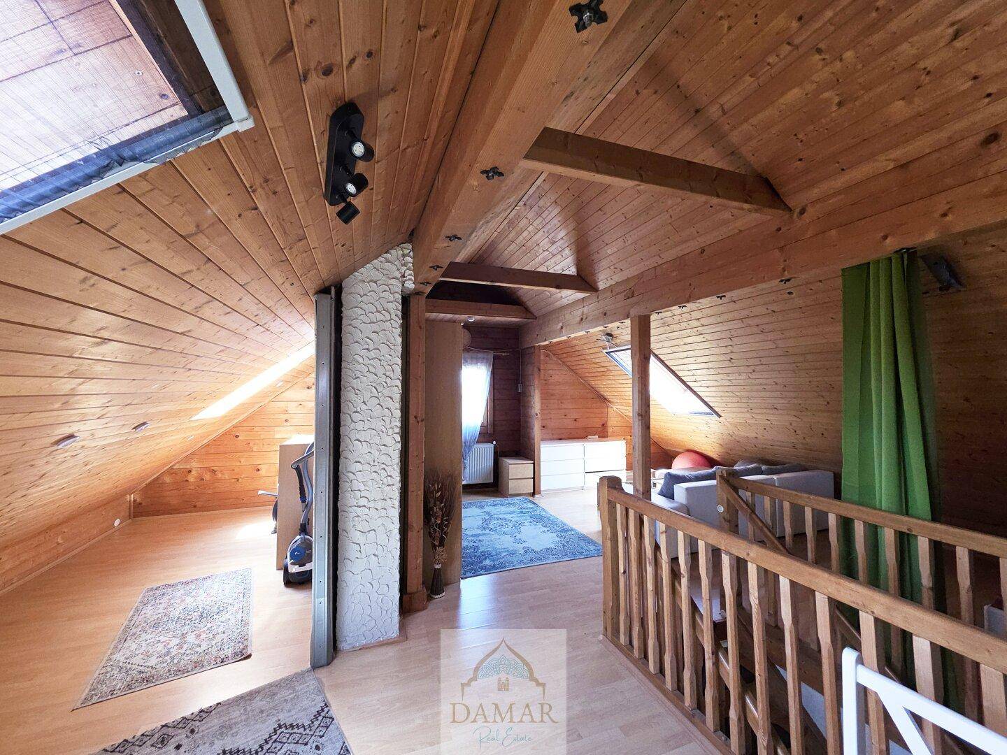 Geräumiger Dachboden als Wohnbereich mit Holzbalken, Dachfenstern und Teppichen.