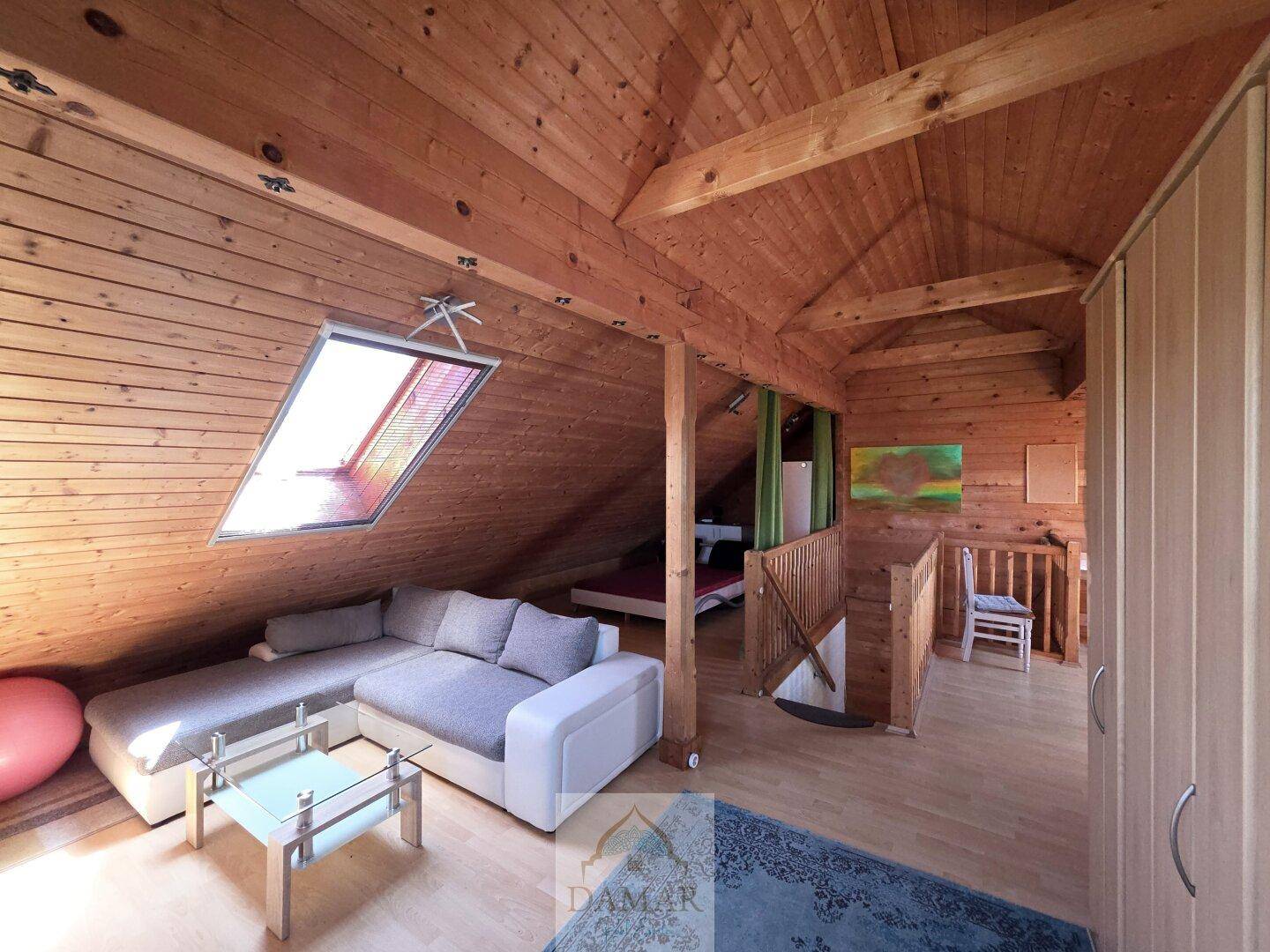 Heller Dachbodenbereich mit Sofa, Couchtisch und Dachfenster, ideal als Rückzugsort.