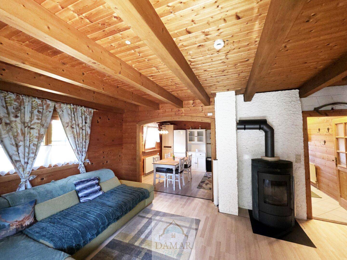 Gemütliches Wohnzimmer mit Holzbalkendecke, Kaminofen und Blick in die offene Küche.