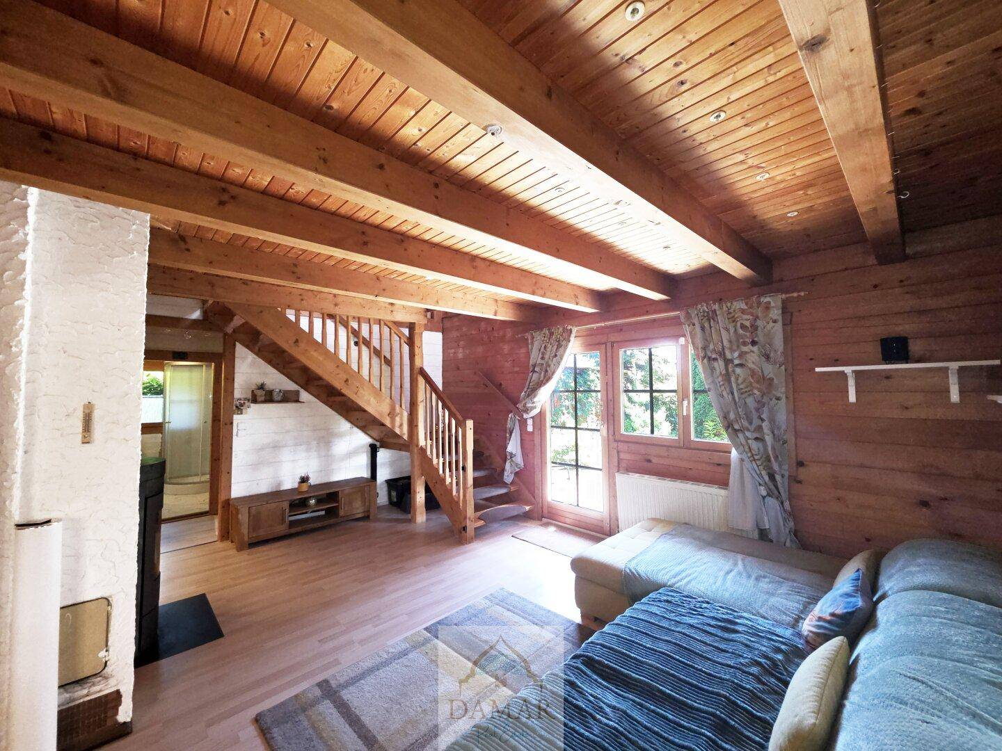 Wohnbereich mit Holztreppe zum Obergeschoss, Holzbalkendecke und Zugang zur Terrasse.