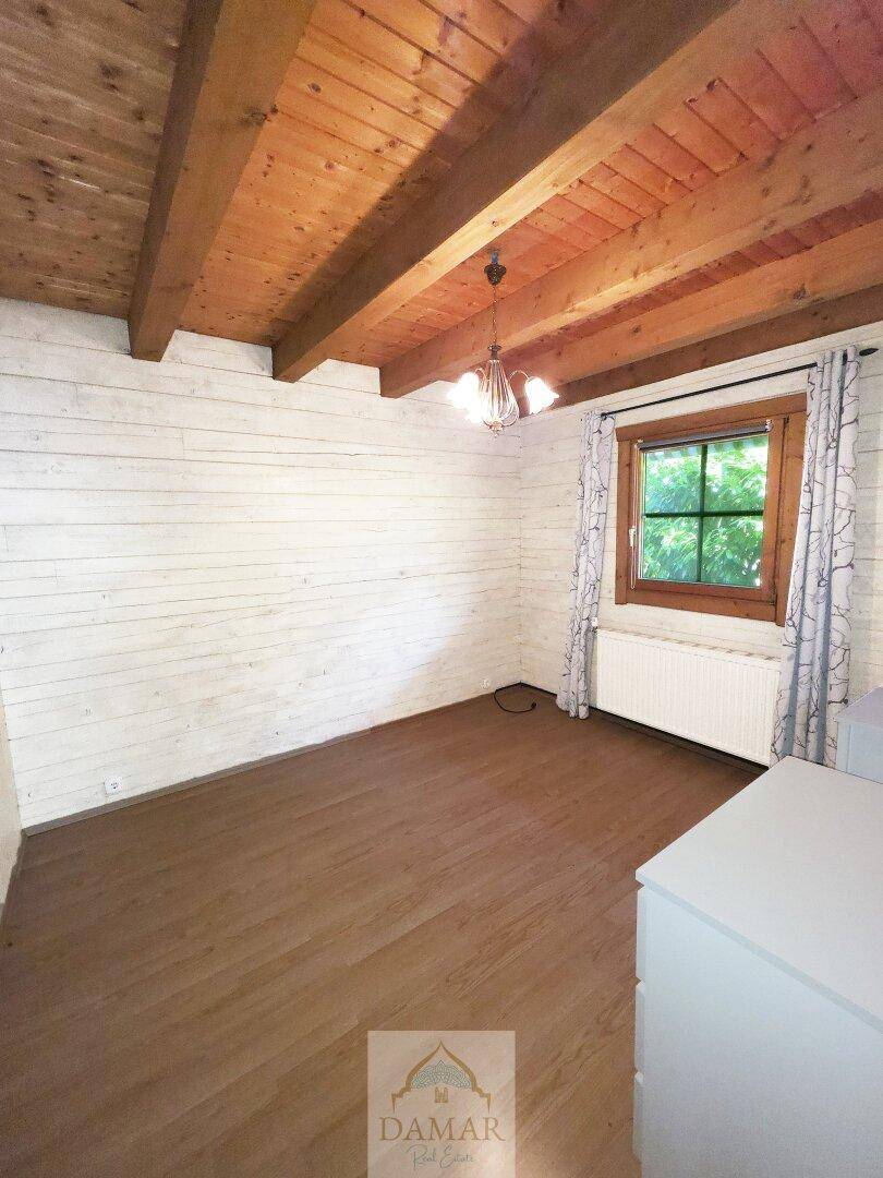 Schlafzimmer mit weiß gestrichenen Holzwänden, Holzbalkendecke und Laminatboden.
