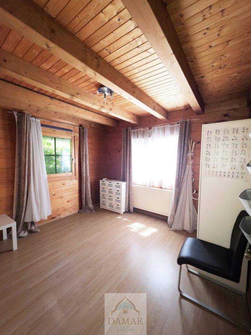 Helles Schlafzimmer mit Holzwänden, Holzbalkendecke und Laminatboden.