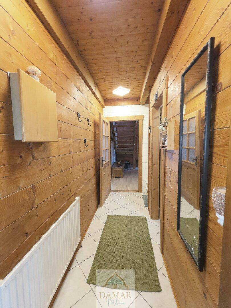 Langer Flur mit Holzwänden, Fliesenboden und Spiegel, der zum Treppenhaus führt.