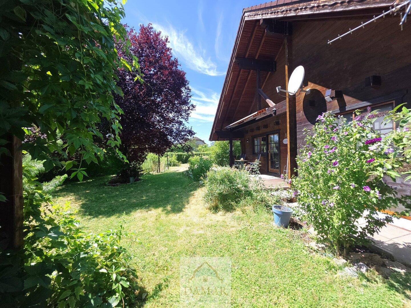 Weitläufiger Gartenbereich neben dem Holzhaus mit üppigem Grün und sonnigem Wetter.