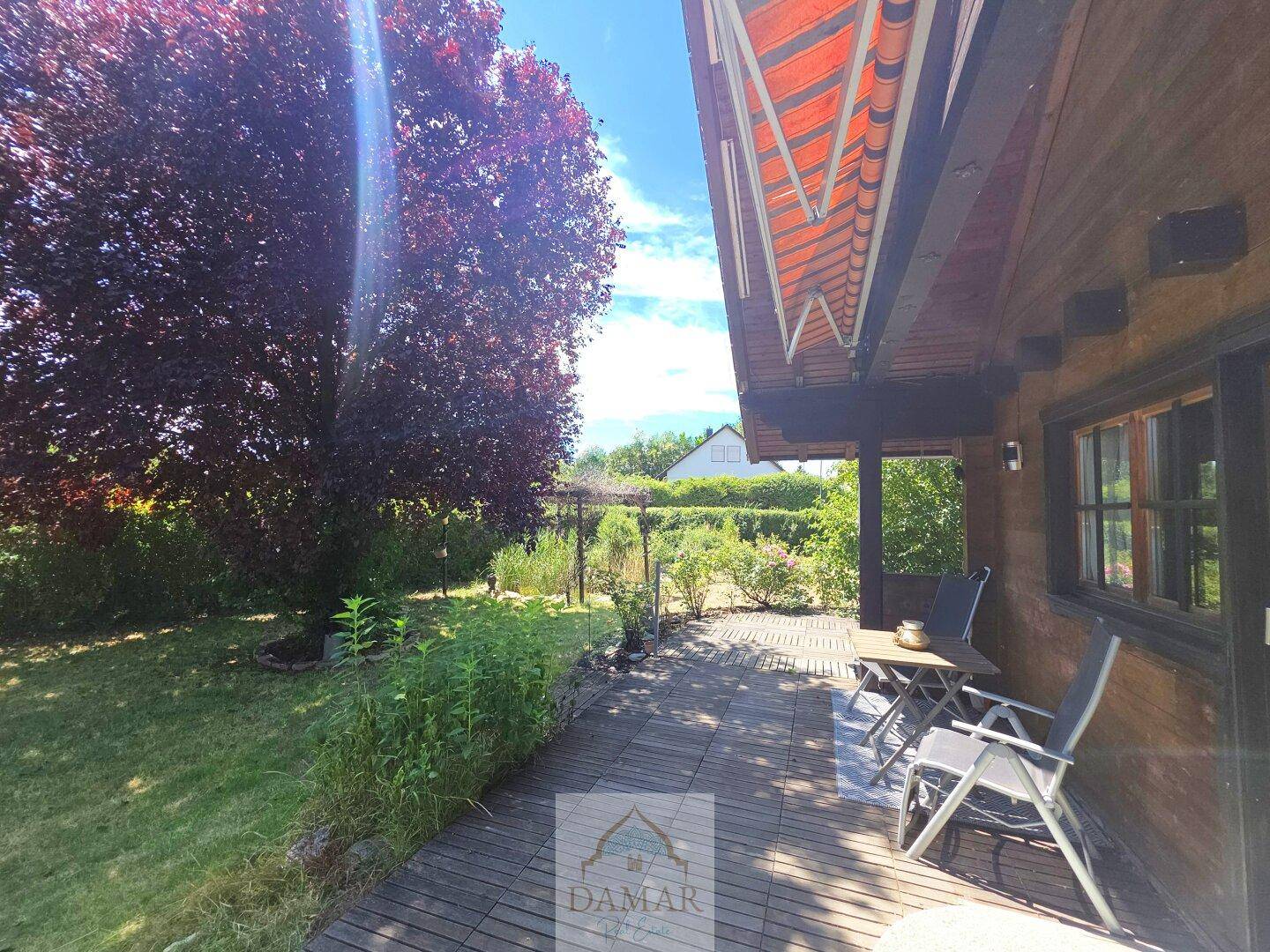 Gemütliche Holzterrasse mit Gartenmöbeln und ausziehbarer Markise für sonnige Tage.